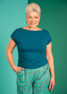 Woman with short blonde hair wearing a wide neck mod teal stretch rayon boat neck top