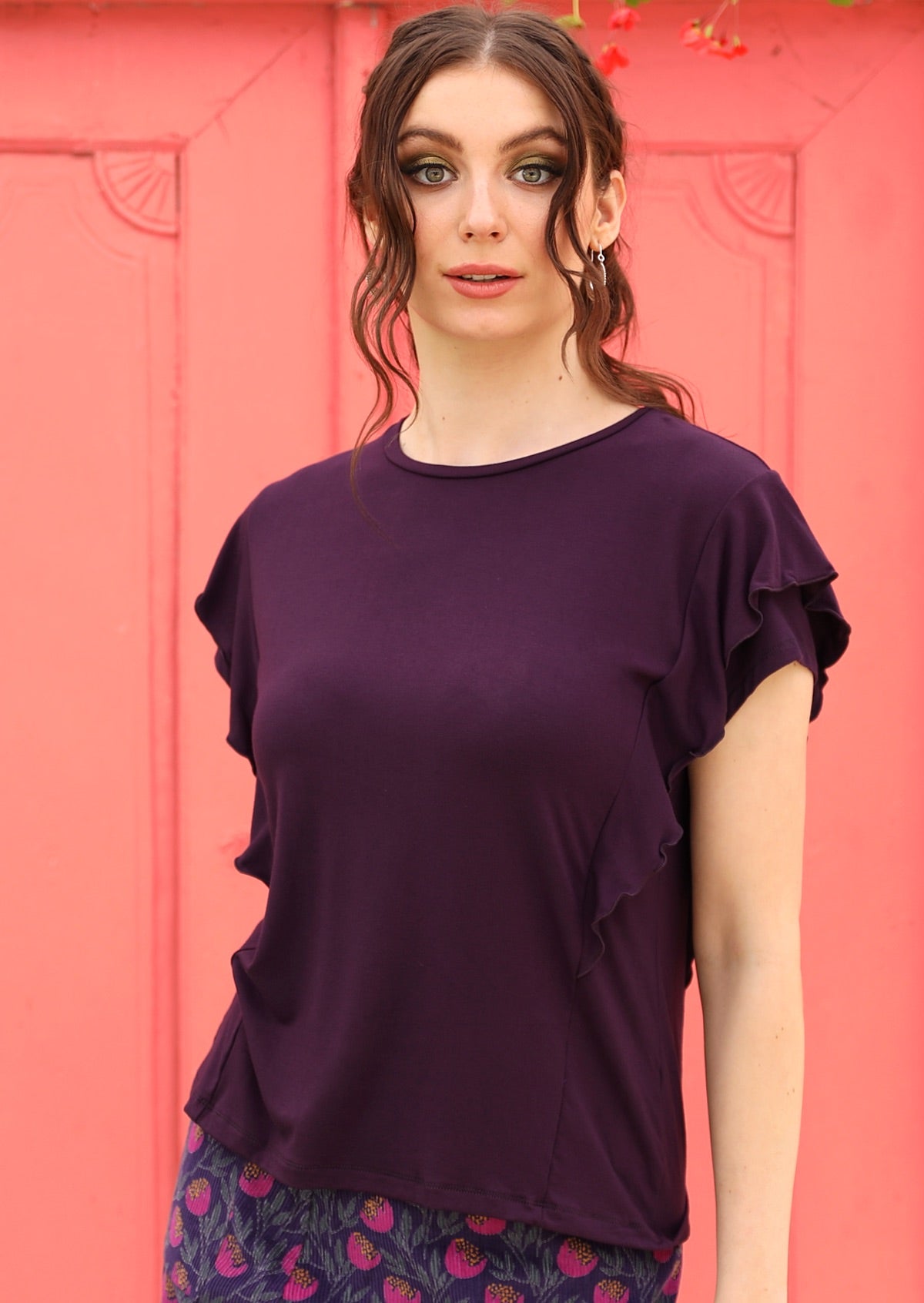Woman wearing a ruffle purple round neck short cap sleeve rayon top with a floral skirt.