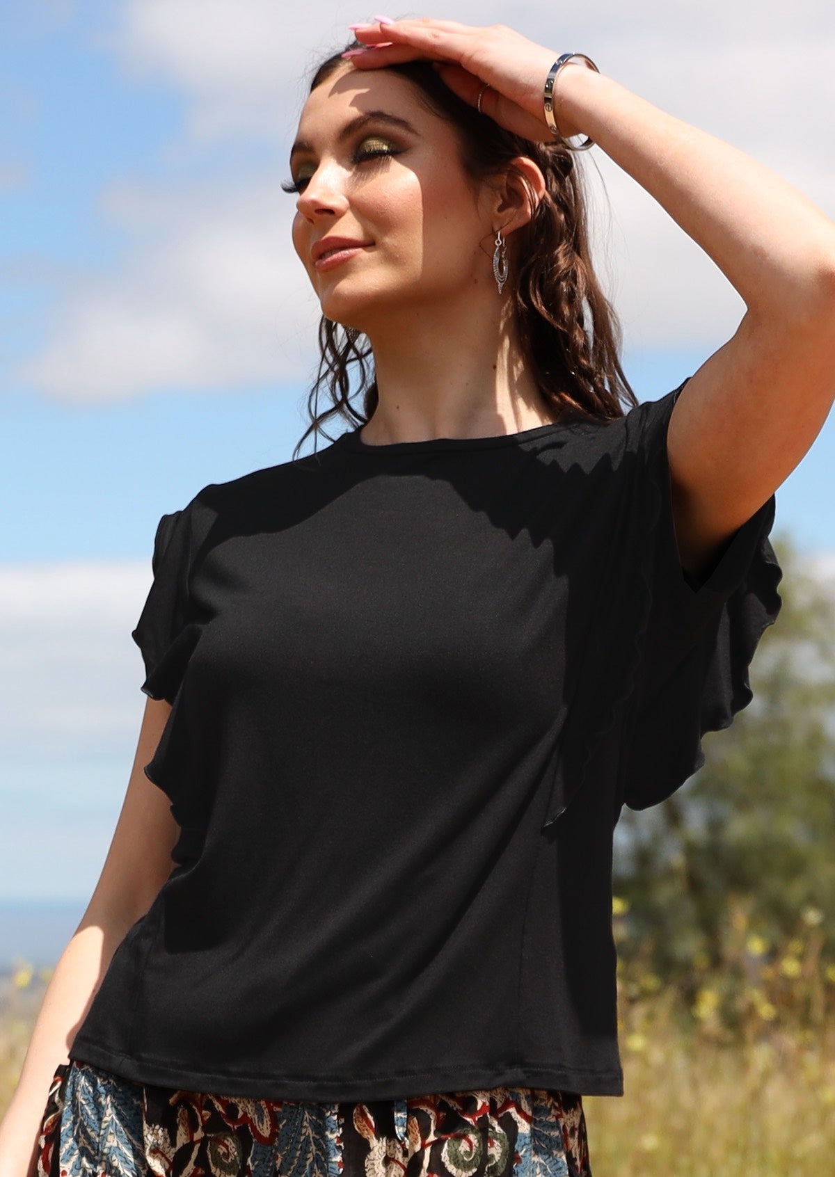 Woman with dark hair wearing a black ruffle round neck short cap sleeve soft stretch rayon top.