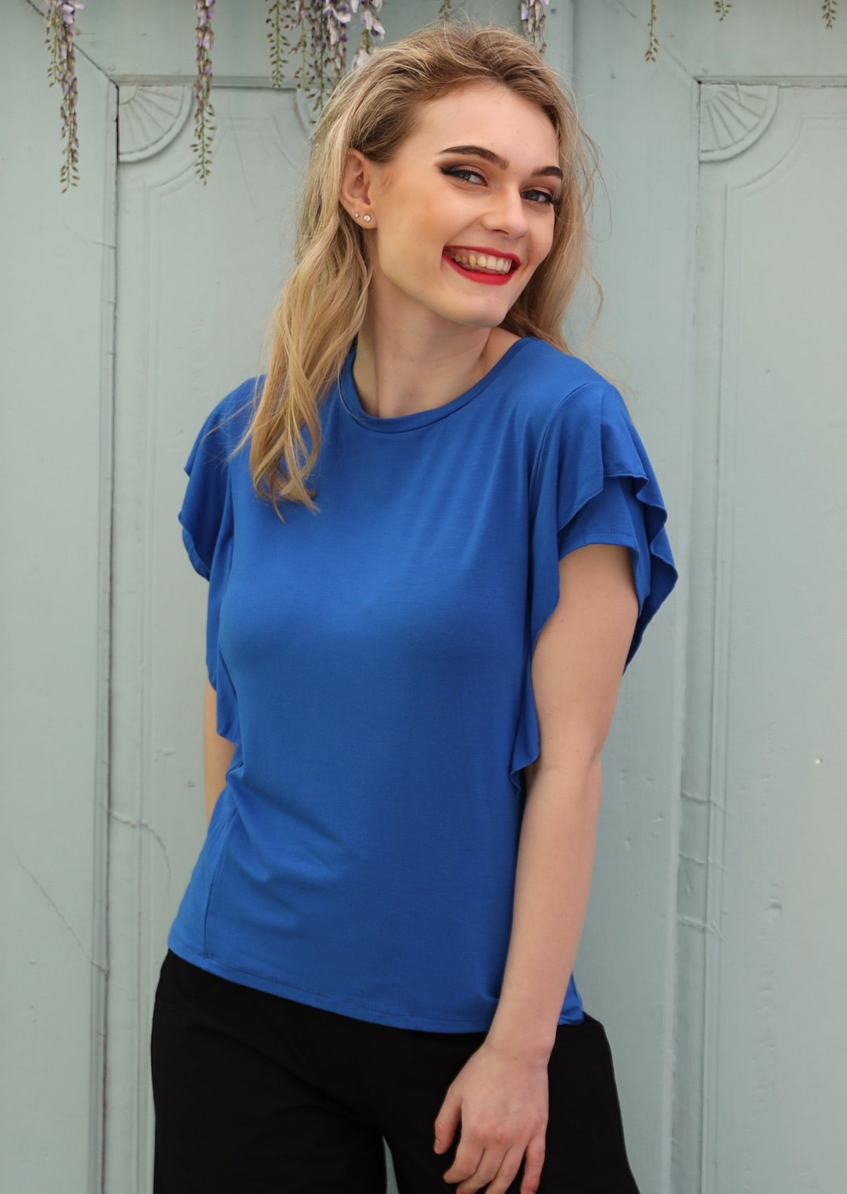 Woman wearing a ruffle electric blue round neck short cap sleeve rayon top.
