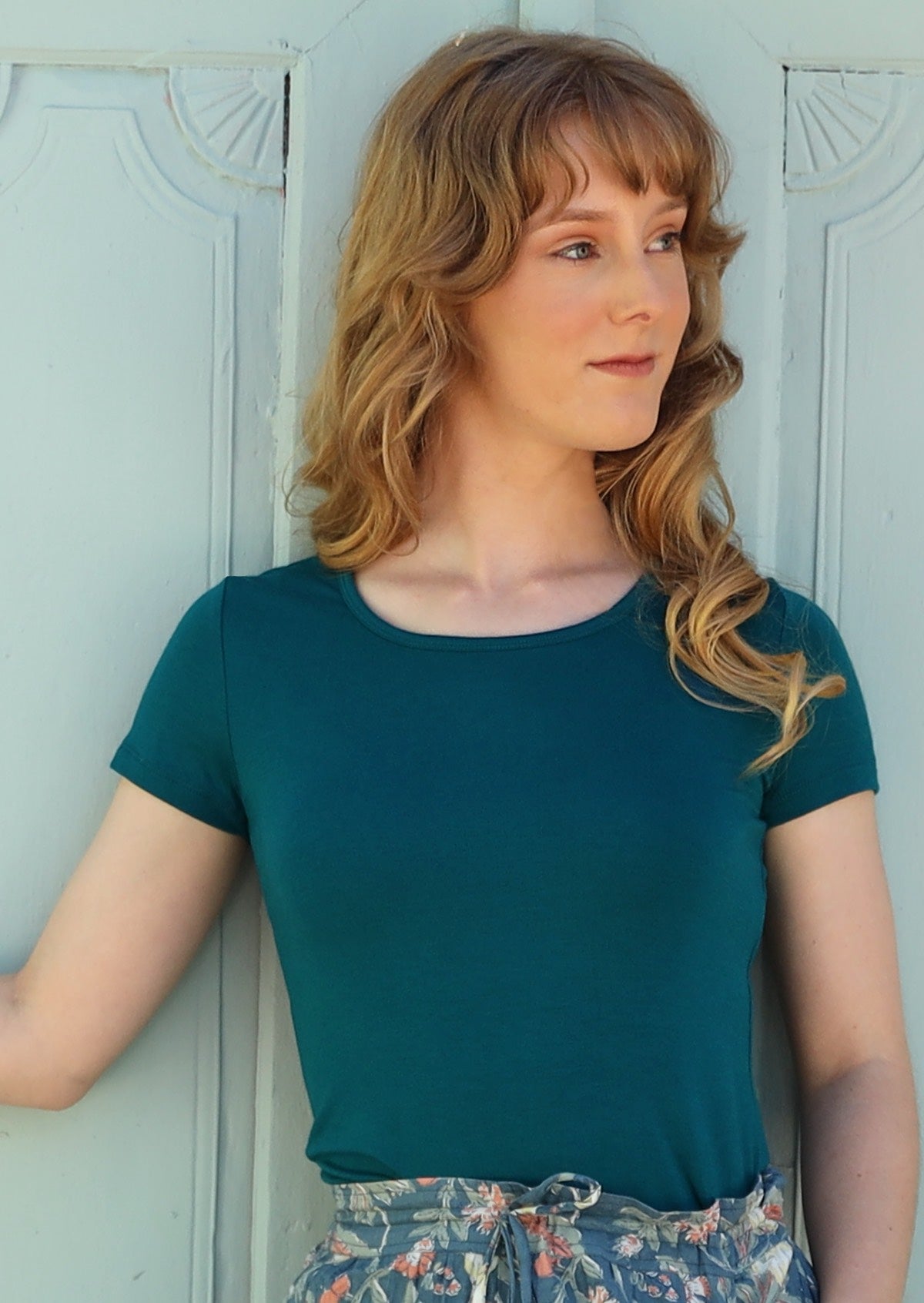 Woman wearing a scoop neck teal rayon fitted t-shirt with green floral pants.