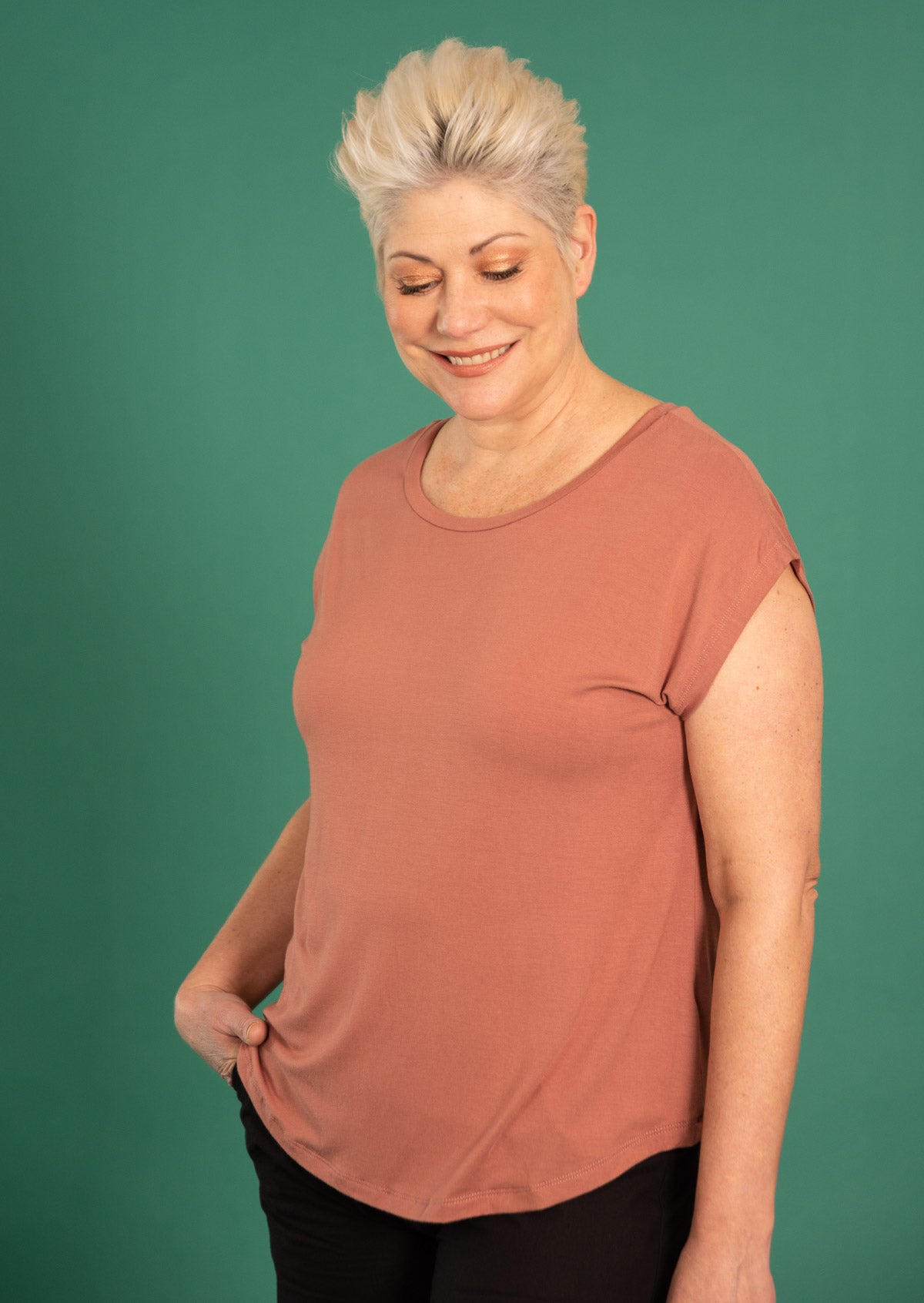 Woman wearing a soft flattering fit dusty pink rayon jersey t-shirt in front of green wall.