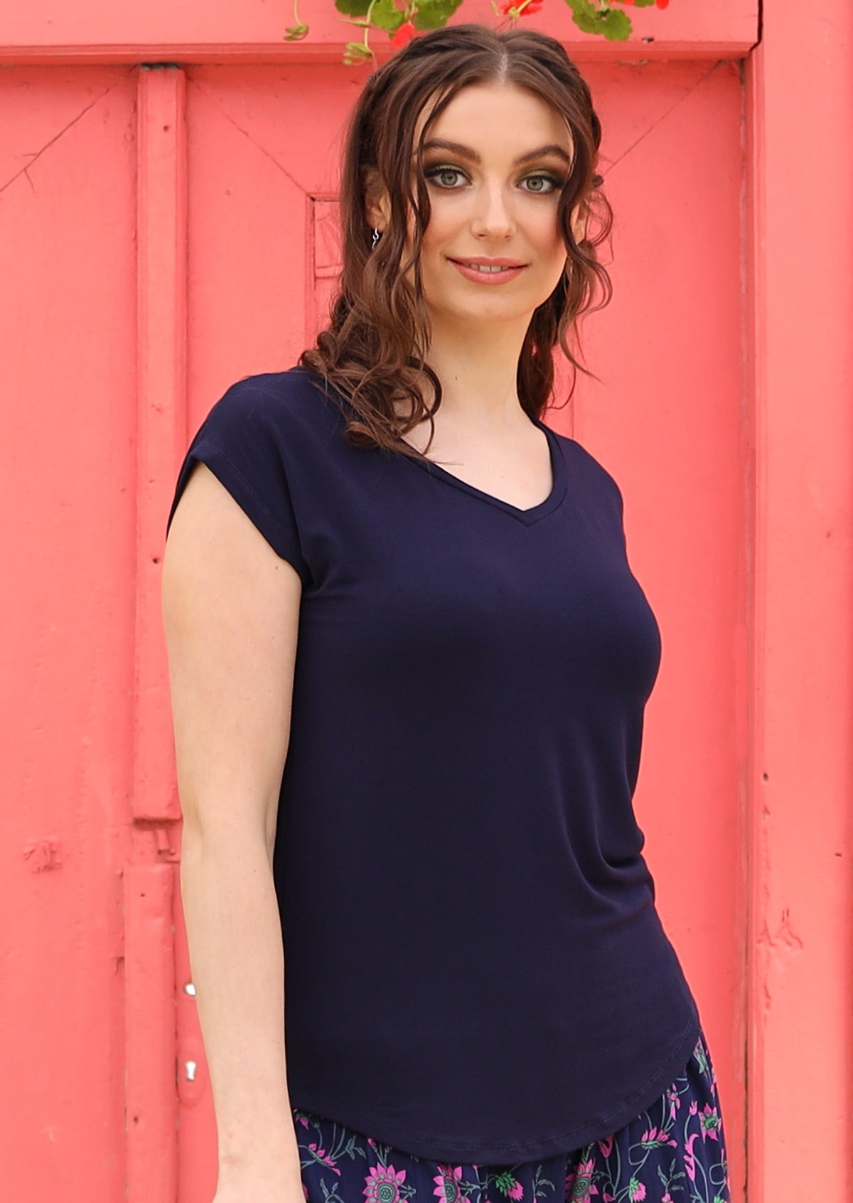 Woman wearing a navy blue v-neck short cap sleeve rayon top in front of a pink wall.