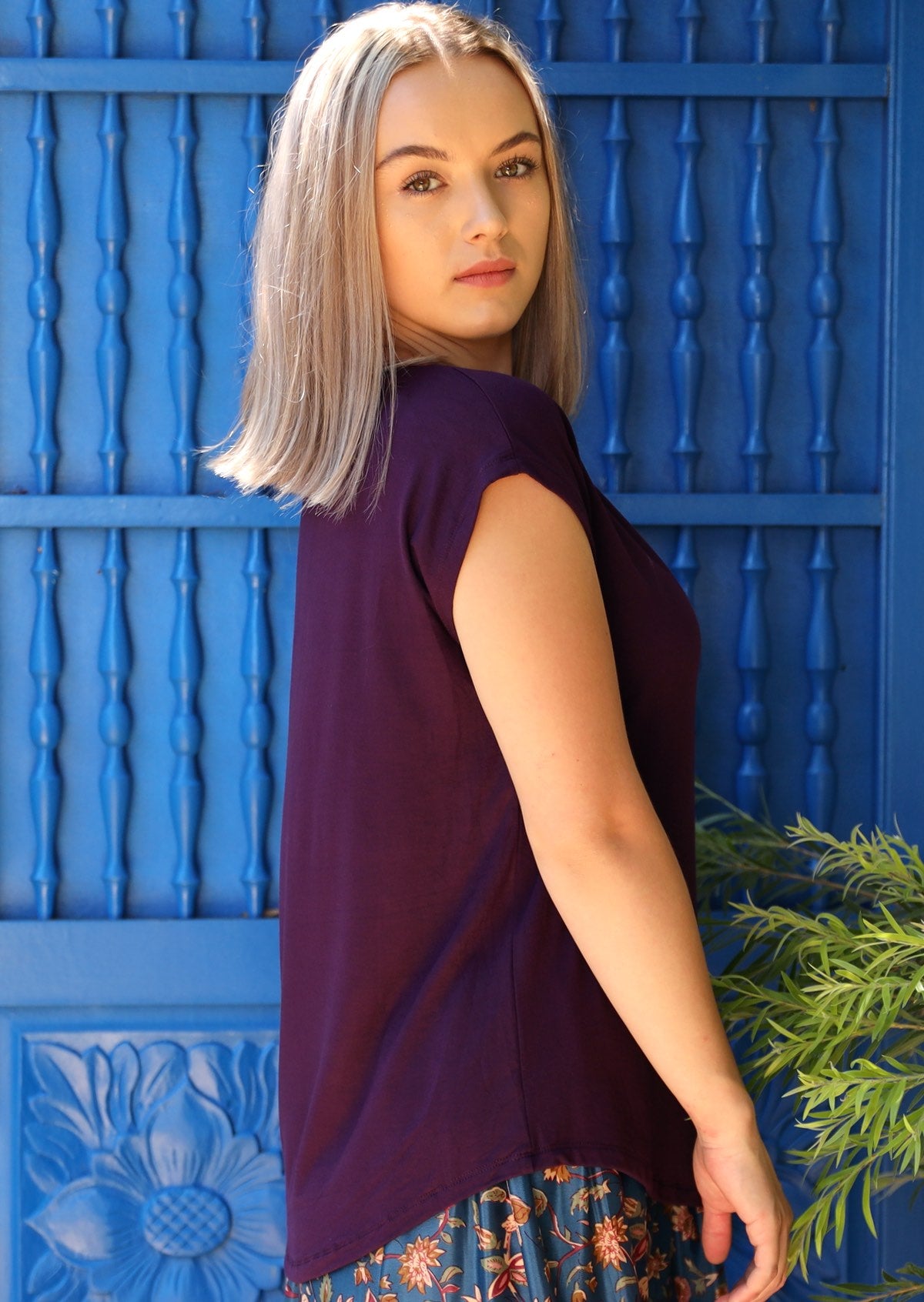 Side view of woman with blonde hair wearing a dark purple v-neck short cap sleeve rayon top