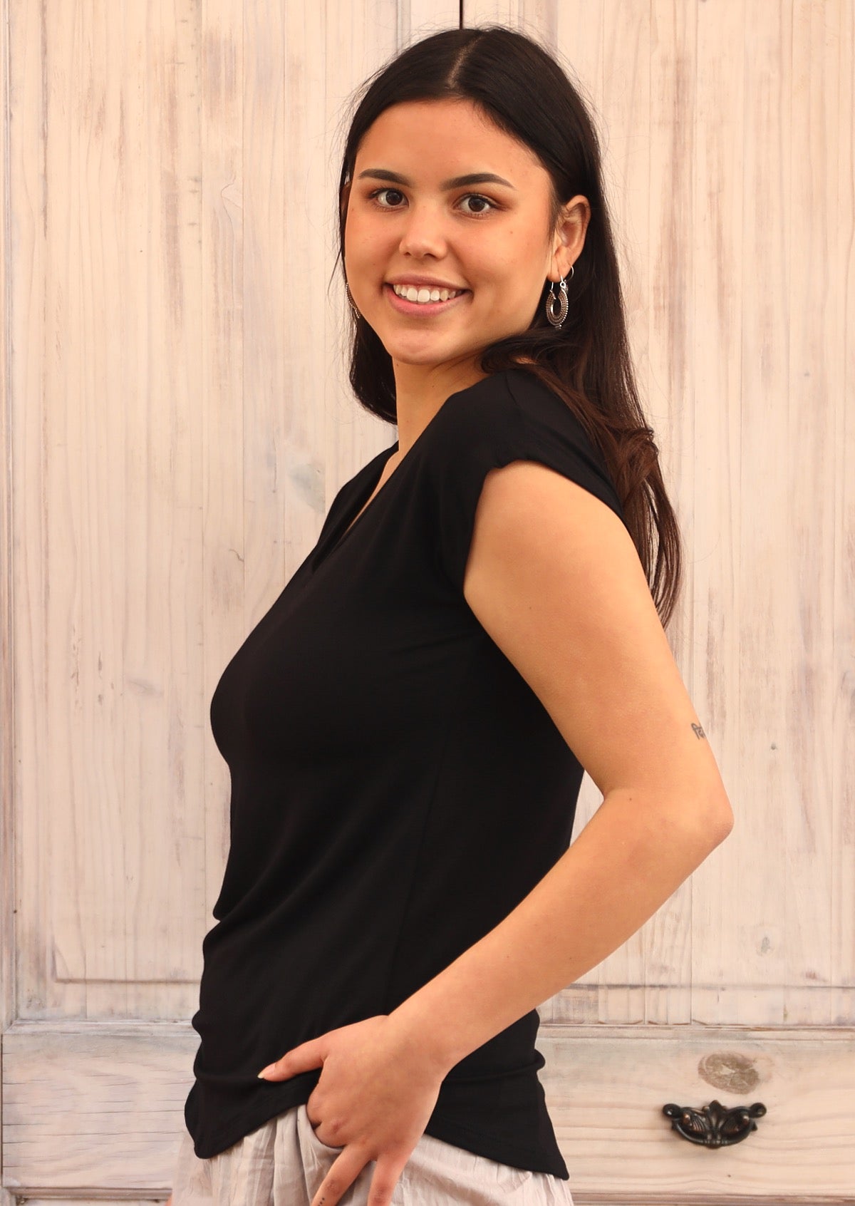 Side view of woman with dark hair wearing a black v-neck short cap sleeve rayon top