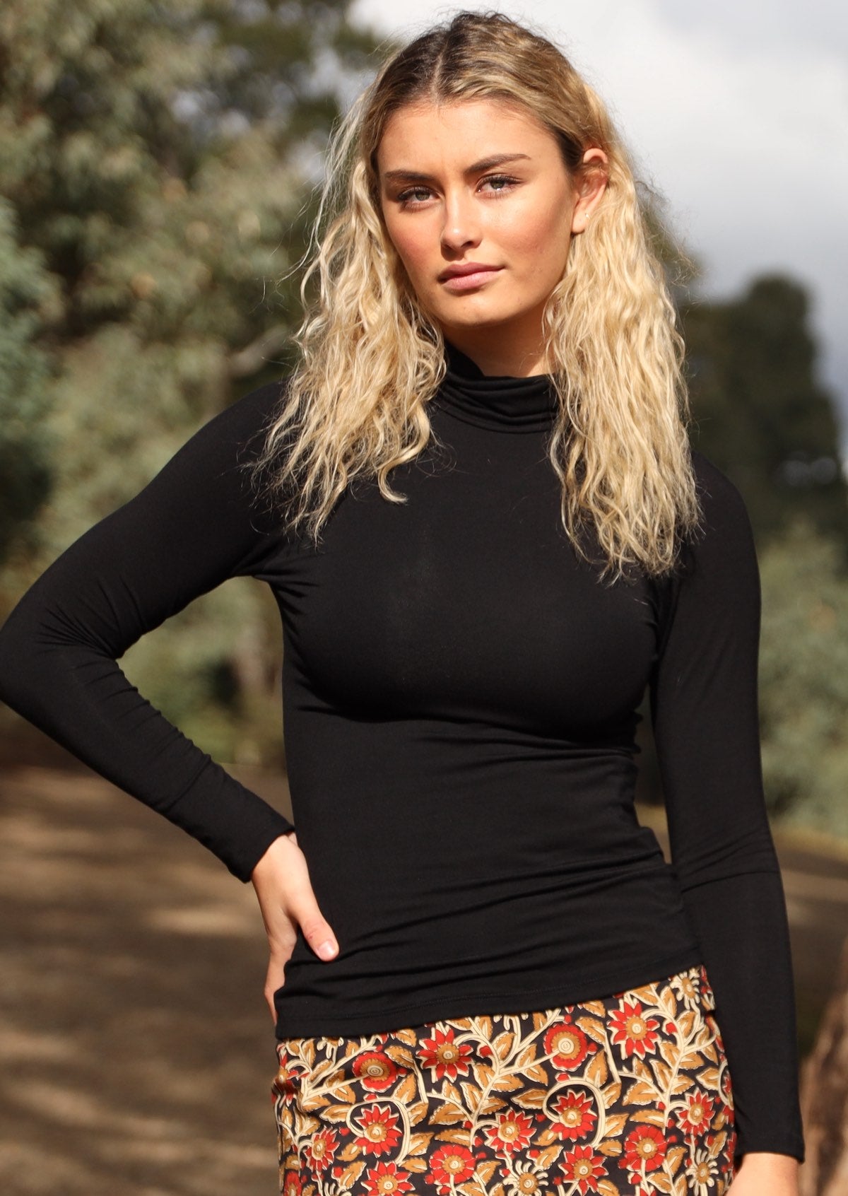 Woman wearing a turtle neck black fitted long sleeve soft stretch rayon top in front of trees.