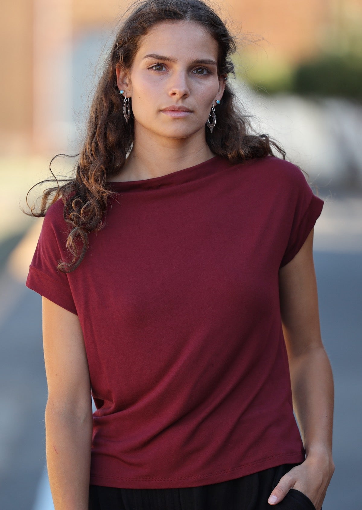 Woman wearing silver earrings and a wide neck mod maroon stretch rayon boat neck top