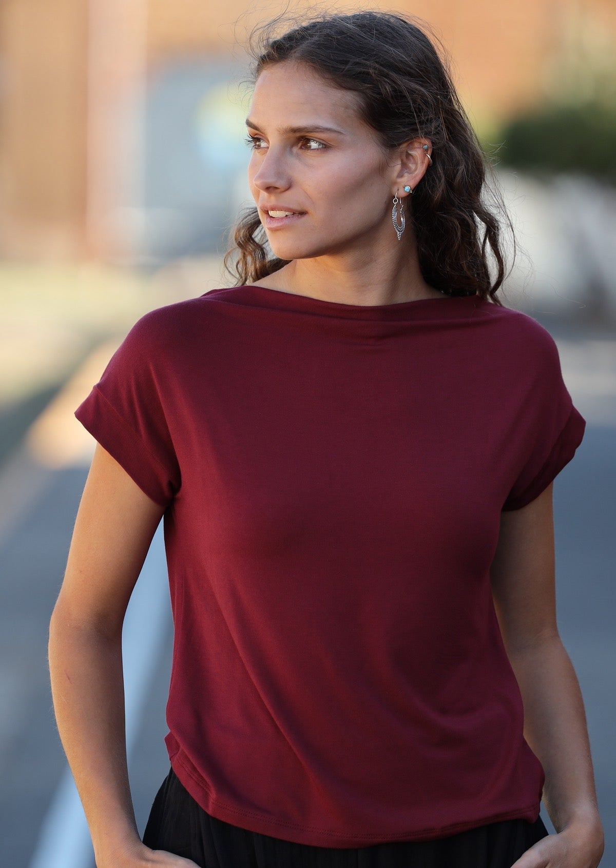 Woman wearing a wide neck mod maroon stretch rayon boat neck top with black pants.