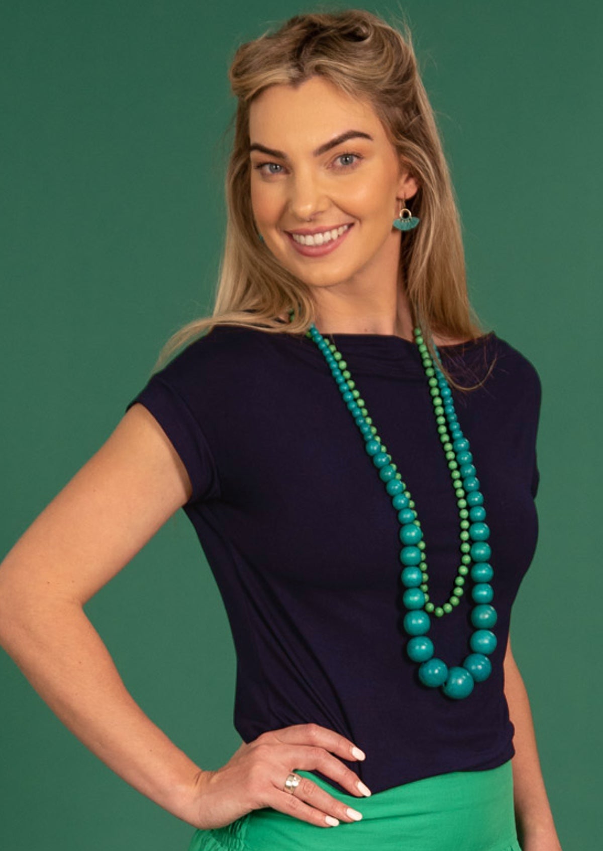Woman with blonde hair wearing a wide neck mod navy blue stretch rayon boat neck top with green beads.