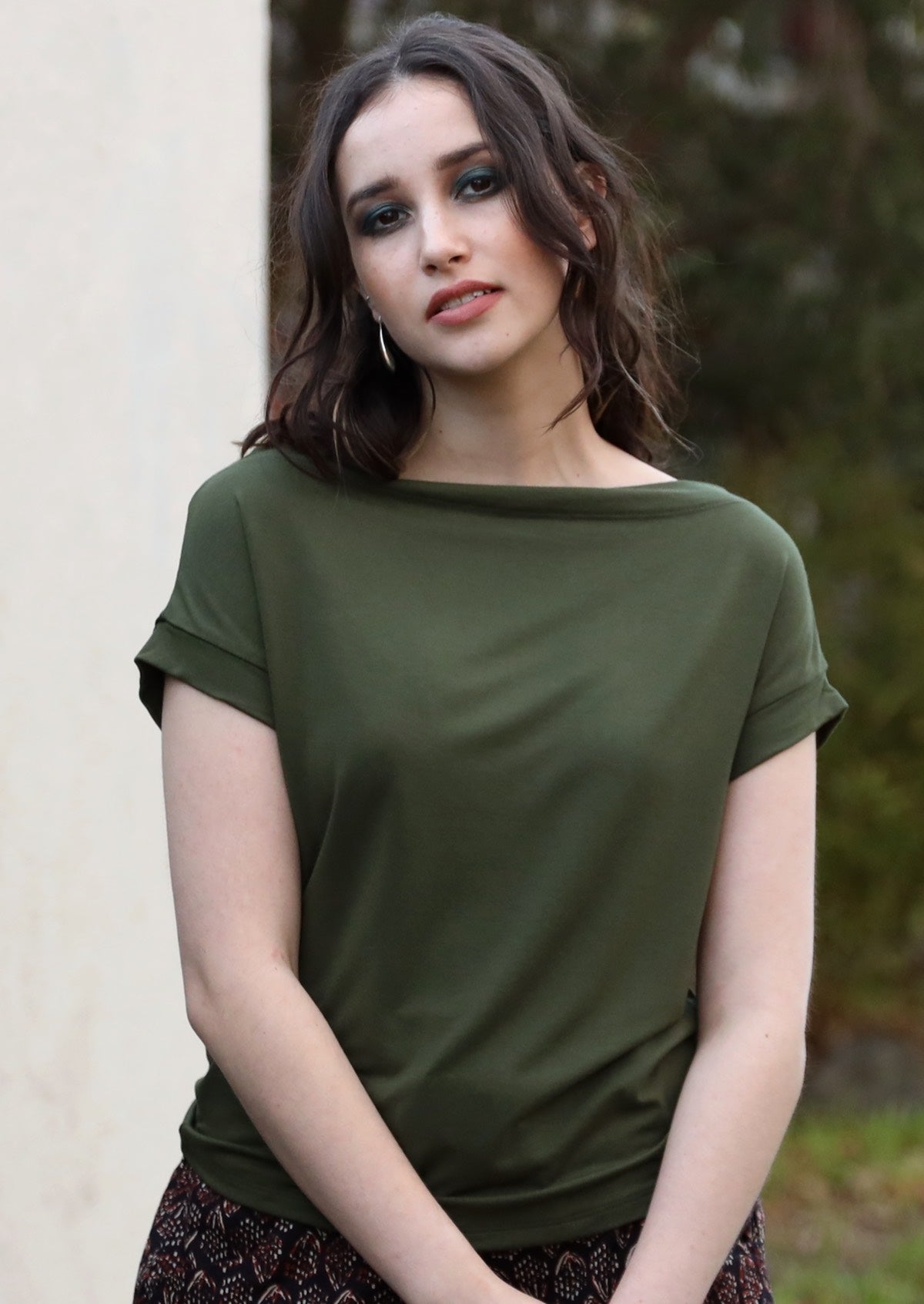 Woman with dark hair wearing a wide neck mod olive green stretch rayon boat neck top.