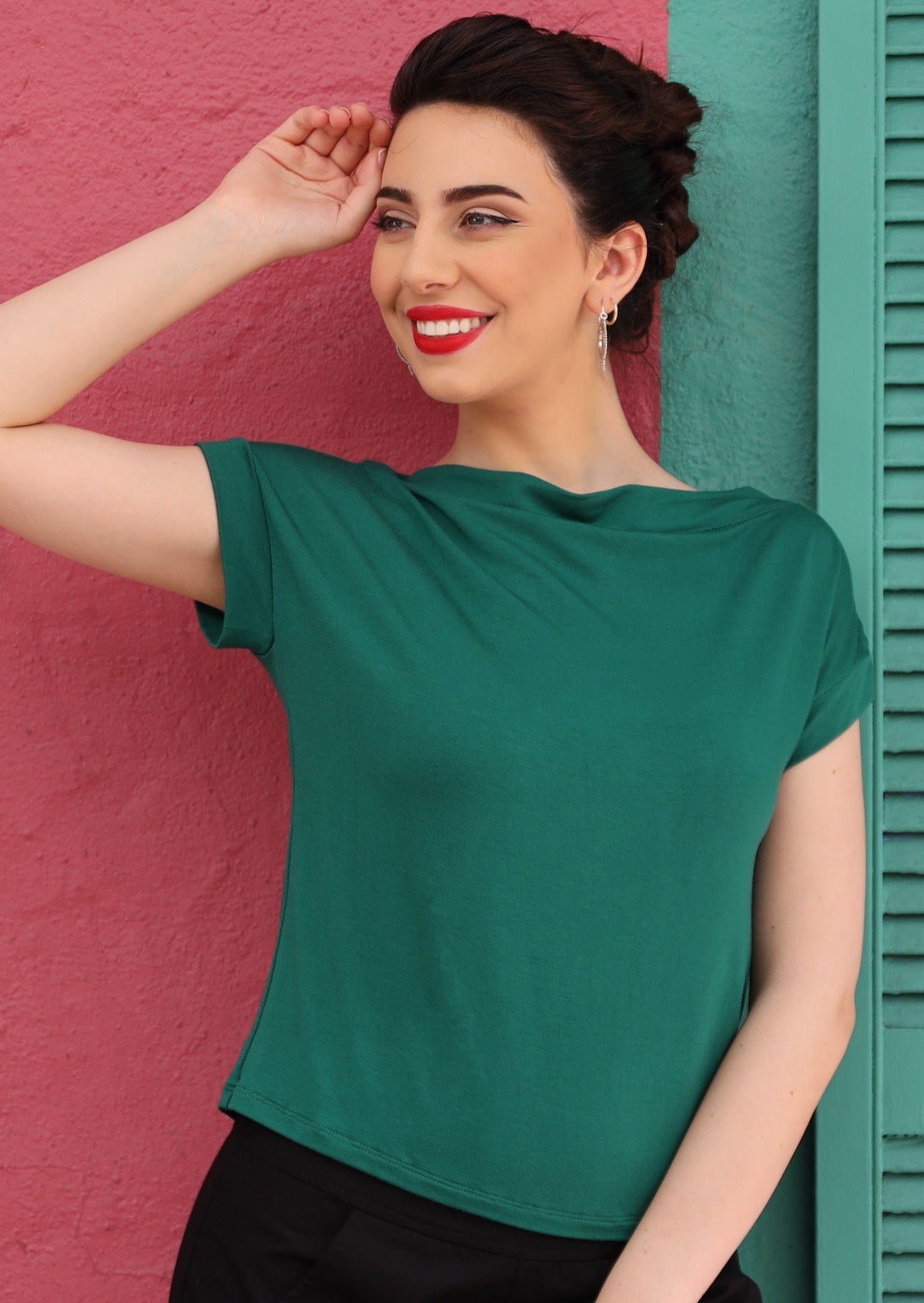 Woman wearing a wide neck mod green stretch rayon boat neck top with black pants.