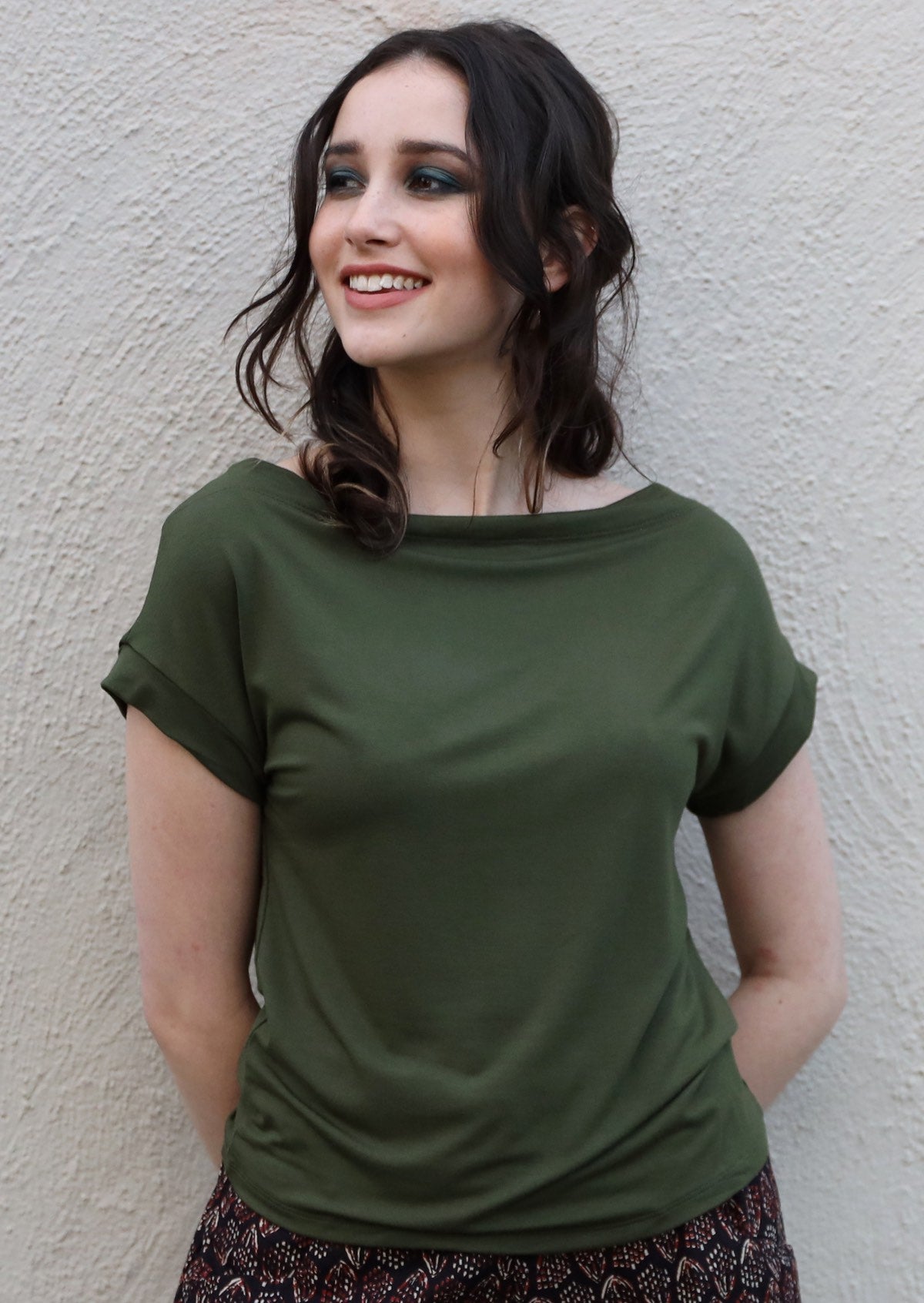 Woman wearing a wide neck mod olive green stretch rayon boat neck top over cream wall.