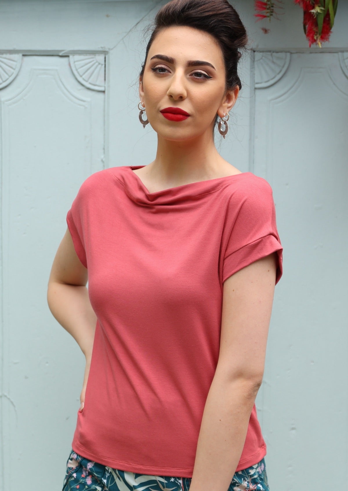 Woman wearing a wide neck mod pink stretch rayon boat neck top in front of a grey door.