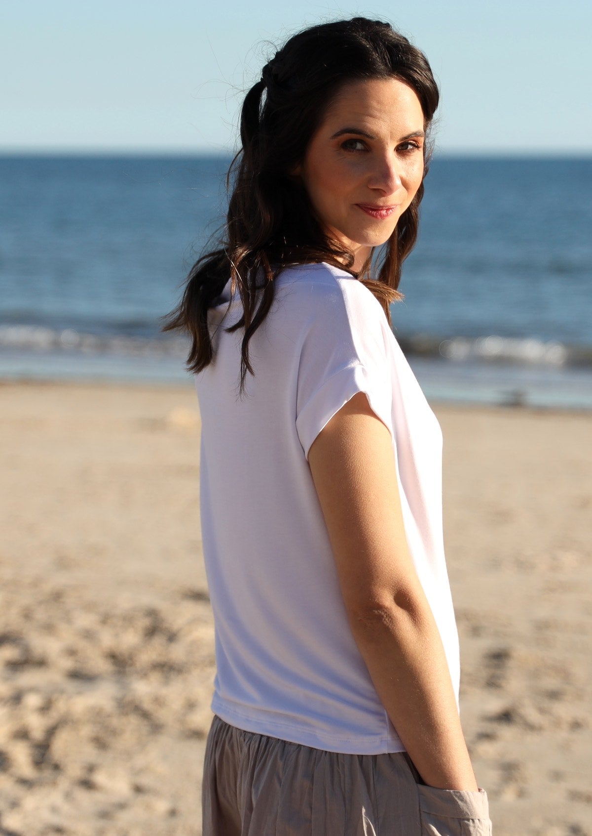 Back view of a woman wearing a wide neck mod white stretch rayon boat neck top