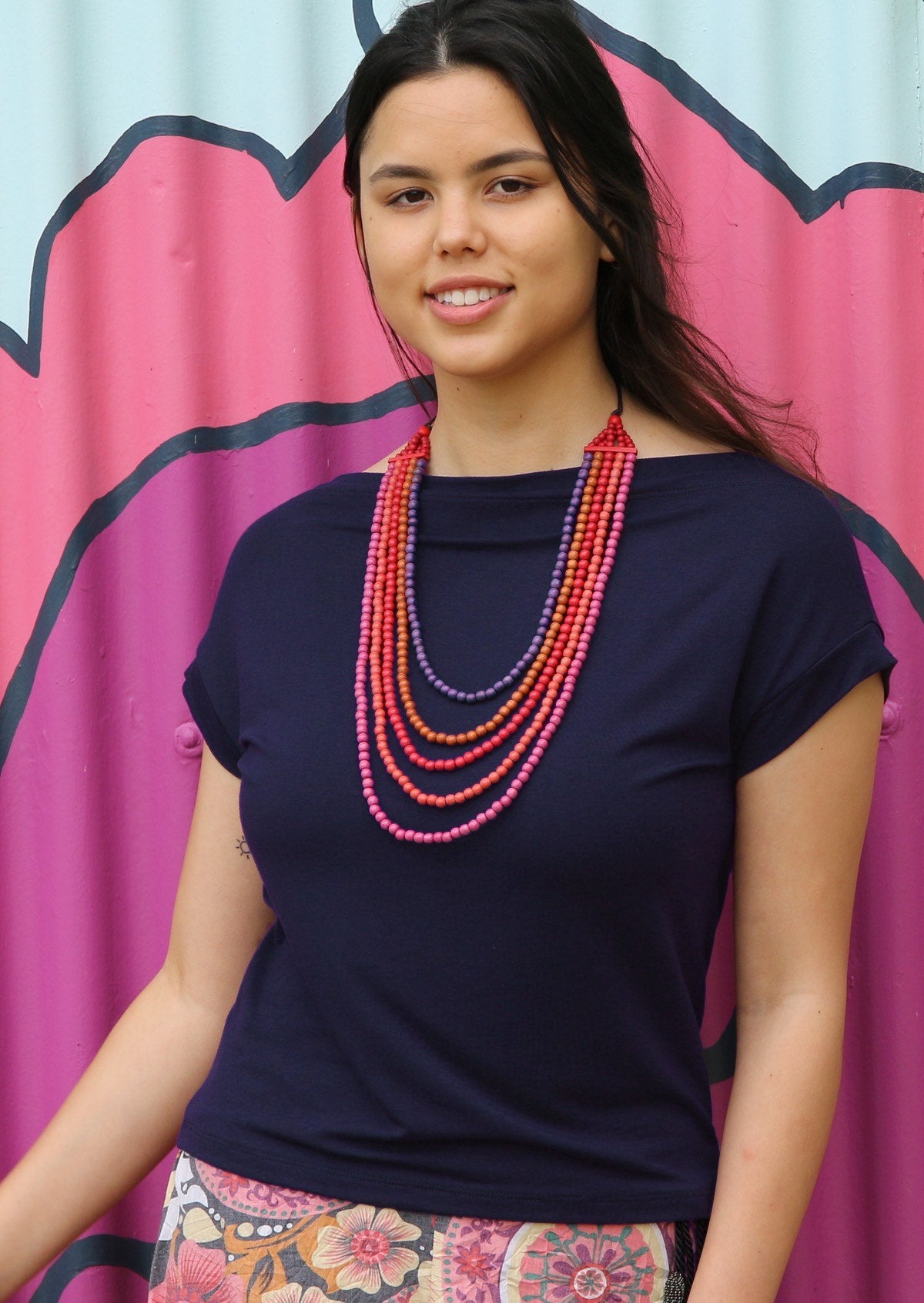 Woman wearing a wide neck mod navy blue stretch rayon boat neck top with colourful bead necklace.
