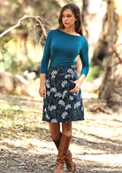 Woman wears A-line corduroy skirt with wide waistband and pockets, in a gorgeous floral print, paired with a teal top