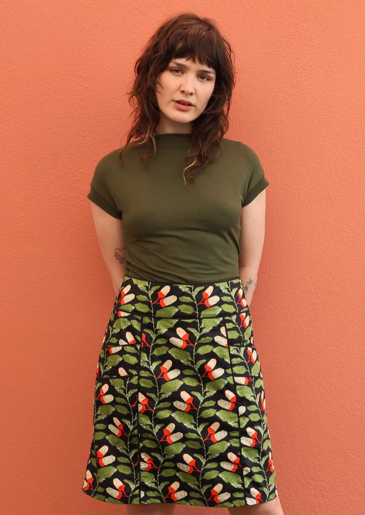 Model wears Aalia Skirt Oak green, orange and white speckled botanical print on black base 100% cotton, knee length A-line skirt with side zip and pockets | Karma East