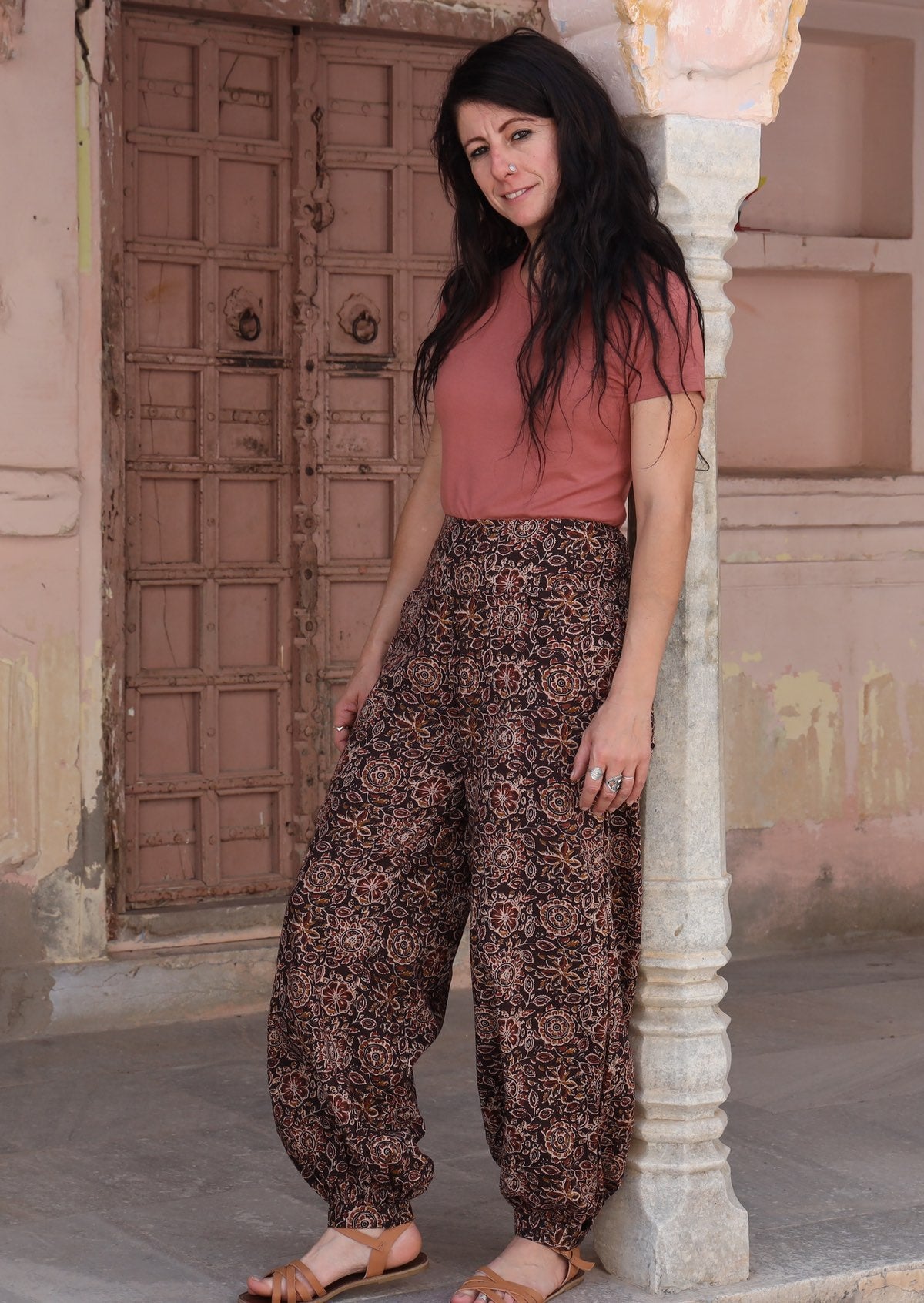 Model stands slightly sideways wearing  wide leg harem pants with buttoned ankle deep pockets and shirring across the back.