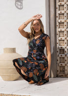 Woman sitting in a floral retro style cotton dress with crossover bodice, cap sleeves and generous skirt.