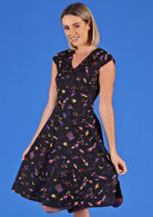 Woman wearing Alice Dress Astro space themed print with black base 50's style dress with V-neck cross over bodice and pockets 