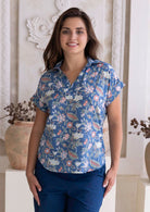 Woman wearing a blue floral cotton top with short folded cuff sleeves, collar and V neckline 