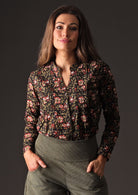 Model in Asha Top Wild Rose black floral print cotton blouse tucked into green corduroy pants