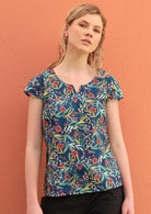 Blonde woman wears a floral top that has a blue base. 