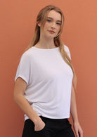 Woman wears white batwing t-shirt with hand in pocket of black pants