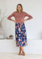Woman wearing a cotton midi length A-line skirt with belt loops in native pink and green floral print.