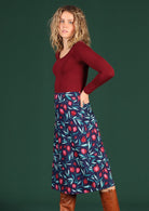 Woman wears 100% cotton navy skirt with a pink and red pomegranate print. This A-line skirt is shin length and has pockets at the back and a hidden side zip