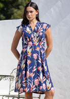 Woman wears  above knee length cotton dress with V neckline, cap sleeves and softly cinched waist.