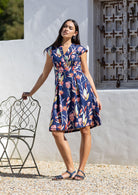 Woman wearing a retro style 100% cotton, floral dress standing outdoors against a white wall.