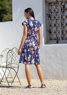 Woman in back pose wears retro style cotton dress with cinched waist, A line skirt and cap sleeves.