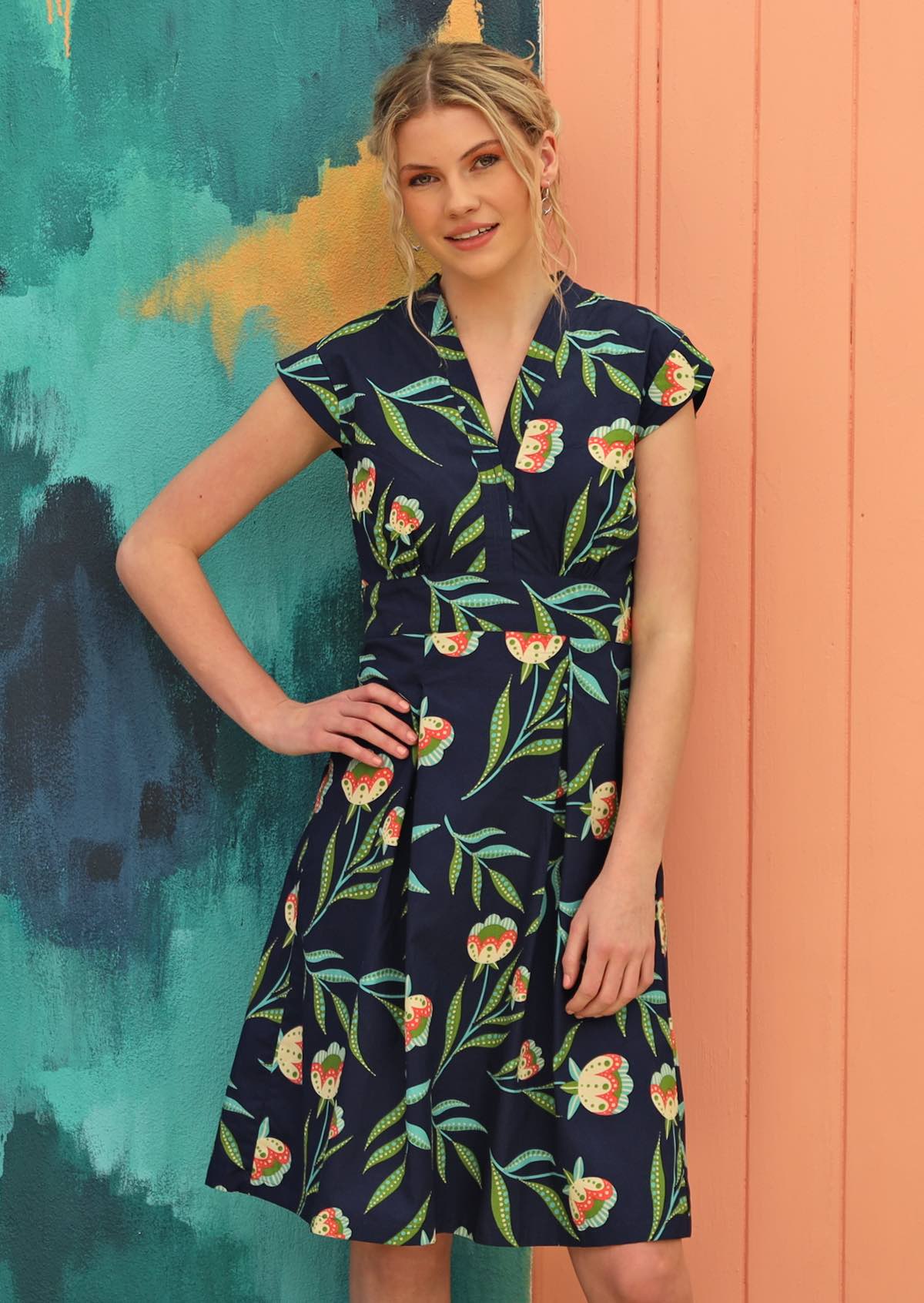 Model wears navy based dress with green floral pattern. 