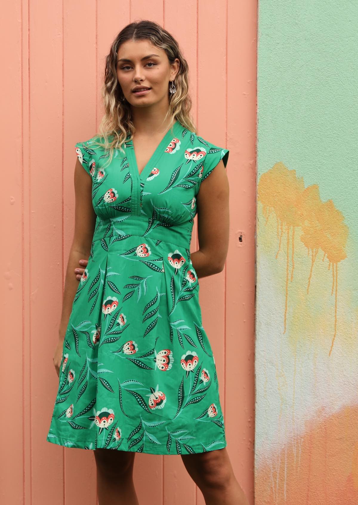 Woman wears floral print dress on a green base. 
