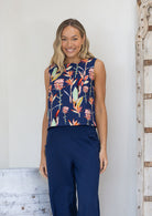 Woman wearing a navy sleeveless cotton top with floral pattern that sits above the hips, paired with navy pants
