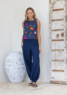 Woman wearing a sleeveless top with colourful polka dots and navy pants with hand in pocket