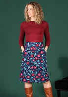 Model wears 100% cotton mid length retro skirt in a blue based pomegranate print featuring piped detail pockets 