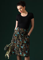 Model wears Bridgette Skirt Thistle black base cotton with botanical print with pops of teal, pencil skirt with plain piping detailing the pockets and yoke | Karma East Australia