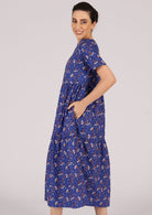 Happy model wears blue based dress with an orange and white floral pattern. 