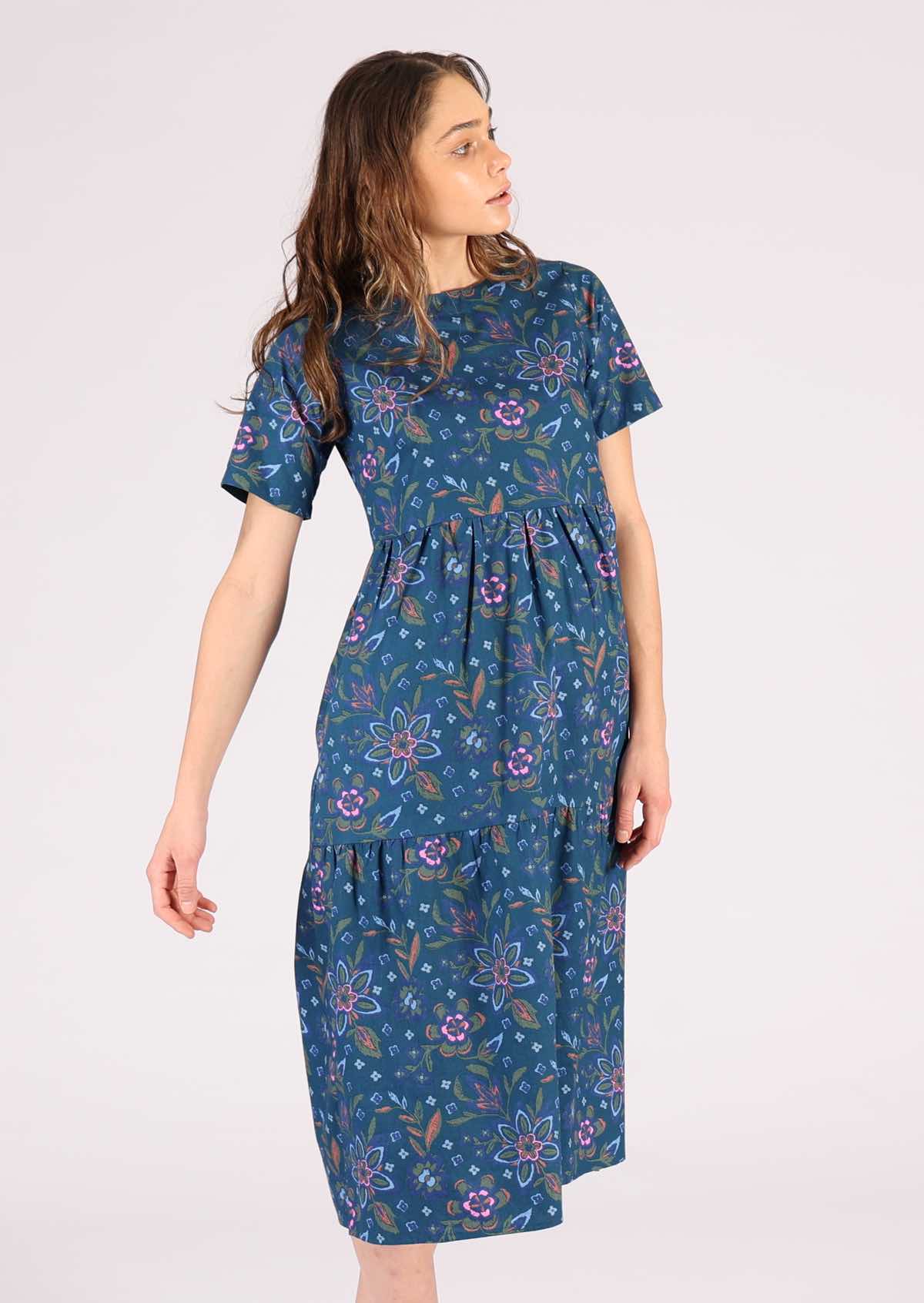 Model wears a blue cotton dress with orange, green and pink florals. 