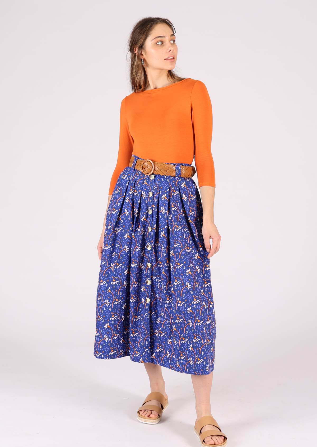 Model pairs blue cotton skirt with a plain long sleeve top, brown belt at the waist and shoes. 