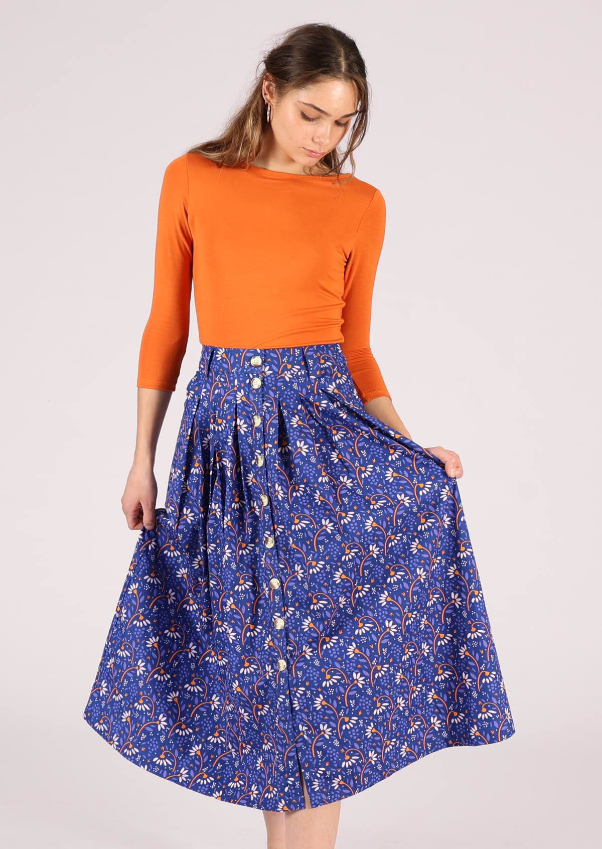 Model wears blue based skirt with a fun orange and off white daisy pattern. 