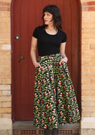 Model wears Cora Skirt Oak green on black print cotton midi length skirt with box pleats, belt loops and pockets | Karma East Australia