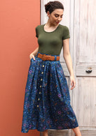 Model pairs blue cotton skirt with a brown belt and short sleeve top. 