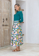 Woman wearing a teal top and pastel print button through skirt with box pleats and pockets