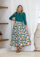 Woman wearing a teal top and pastel print shin length skirt with box pleats and belt loops
