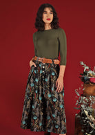 Model wears Cora Skirt Thistle botanical print with pops of teal on black base cotton, box pleated waistband with belt loops and pockets, A-line shin length skirt | Karma East Australia