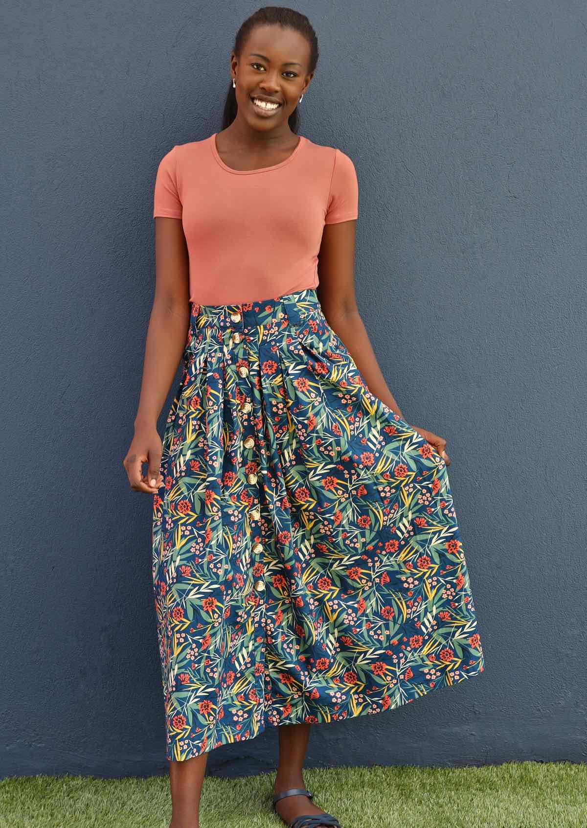 Model poses in cotton floral skirt with box pleats and button down front centre