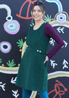 Model wears Cord Button Dress round neck sleeveless form fitting bodice a-line skirt adjustable side buttons non-functional shoulder buttons back pockets 100% cotton corduroy green | Karma East Australia